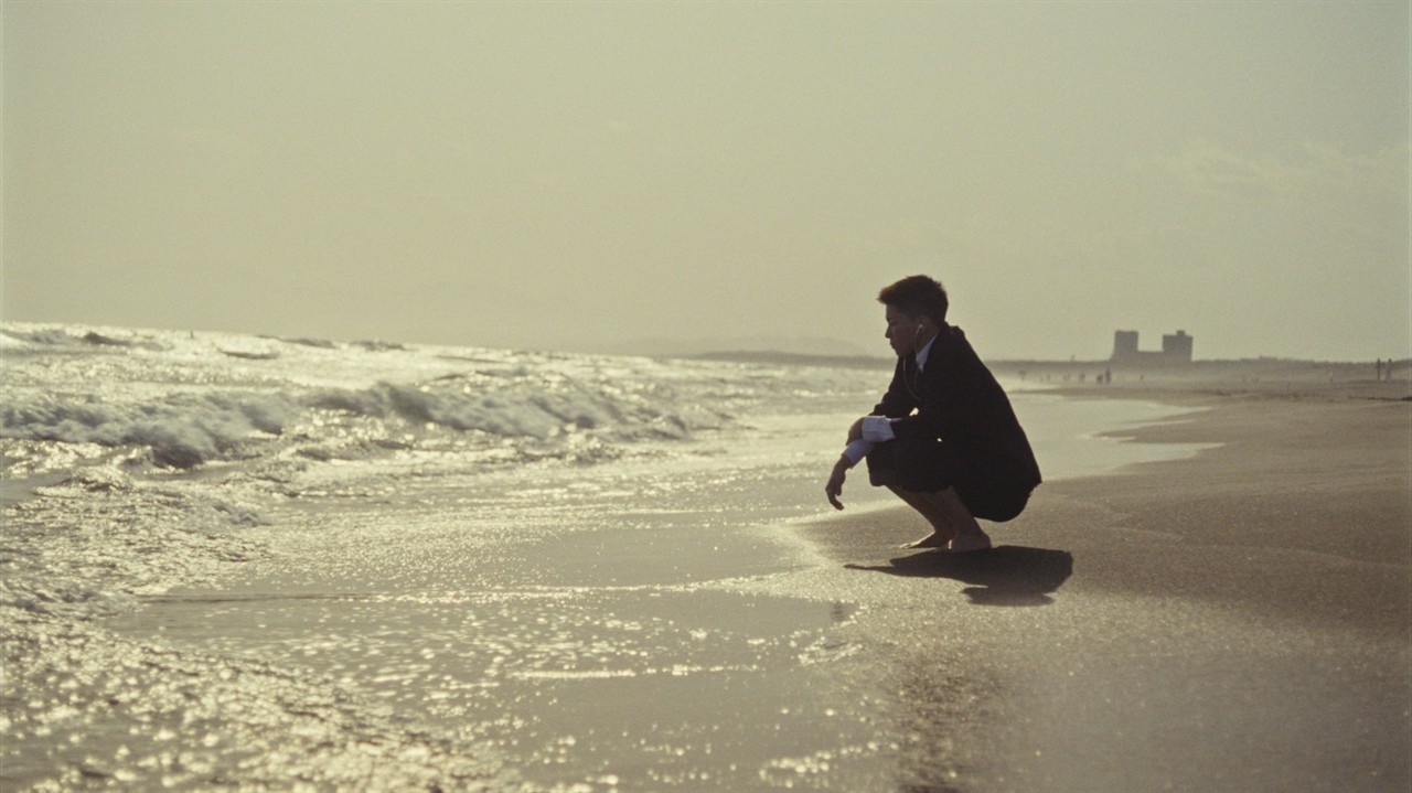 Person crouching at the edge of an ocean